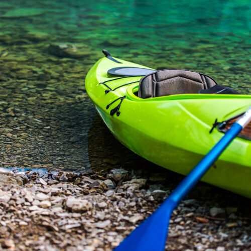 Kayaking on the Lake Concept Photo. Green Sport Kayak on the Rocky Lake Shore. Closeup Photo.